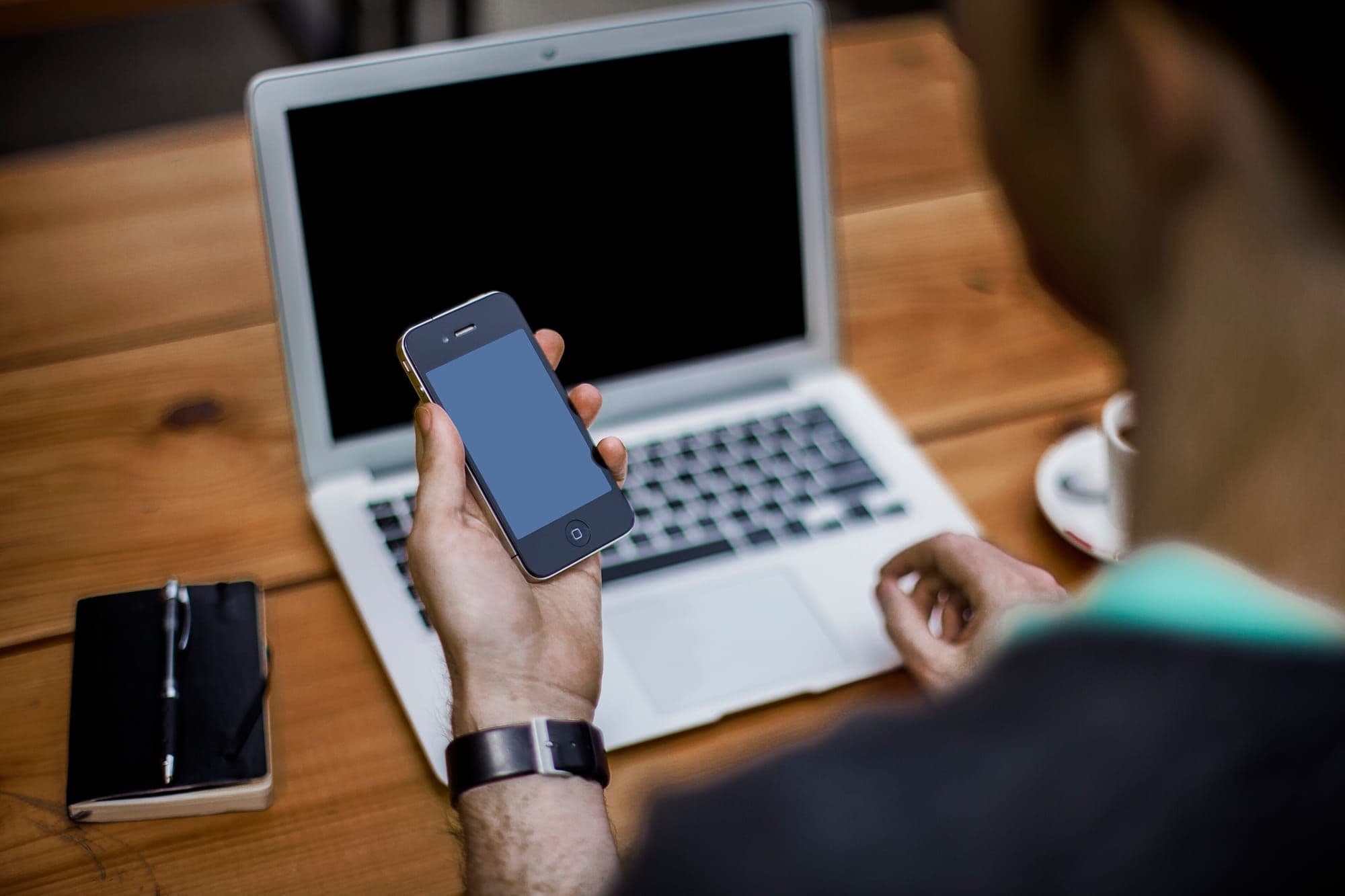 Hand holding a phone beside an open laptop and notebook